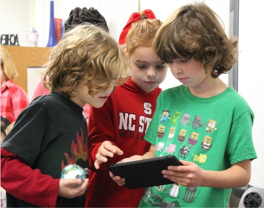 Three young kids working together using device and robot