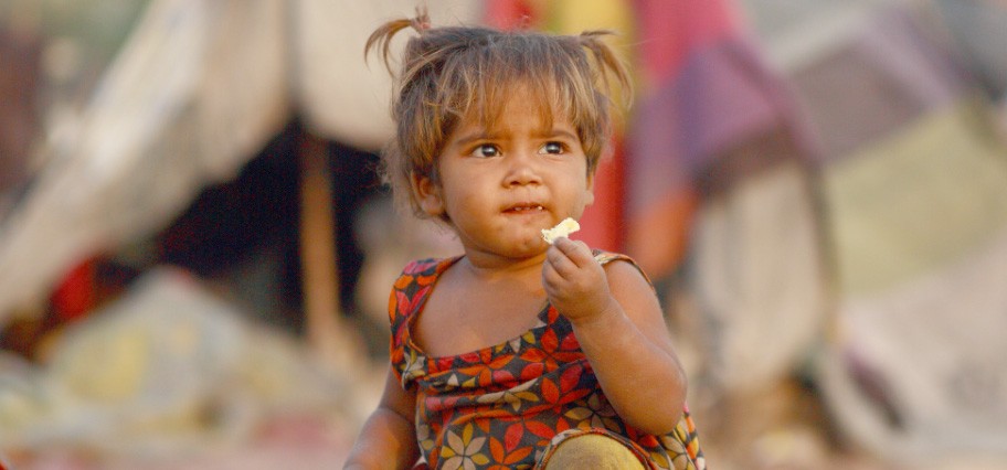 Very young girl in a flowered shirt holding food in her hand